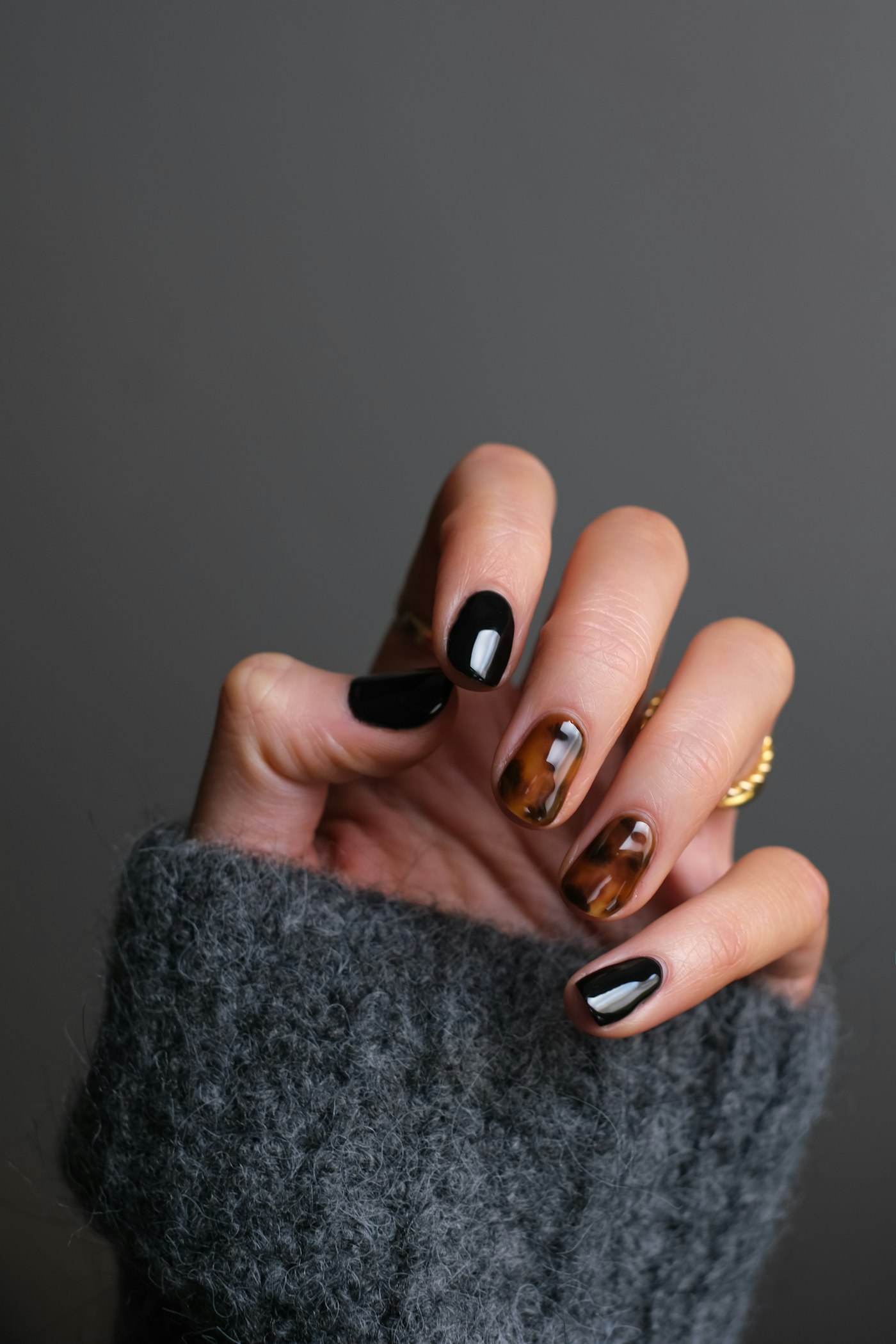 Hand with glossy black and tortoiseshell manicure wearing a gold ring
